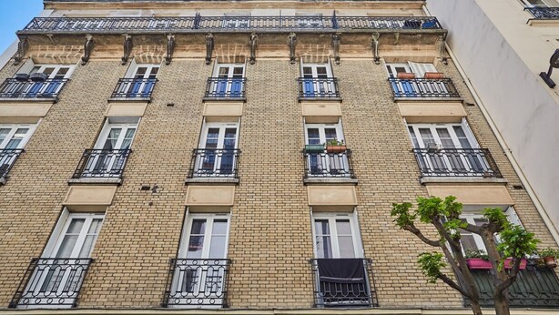 A multi-story building with a brick facade, multiple balconies with black railings, and a tree in the foreground. - Apartment Paris Exposition Park Center (Paris)