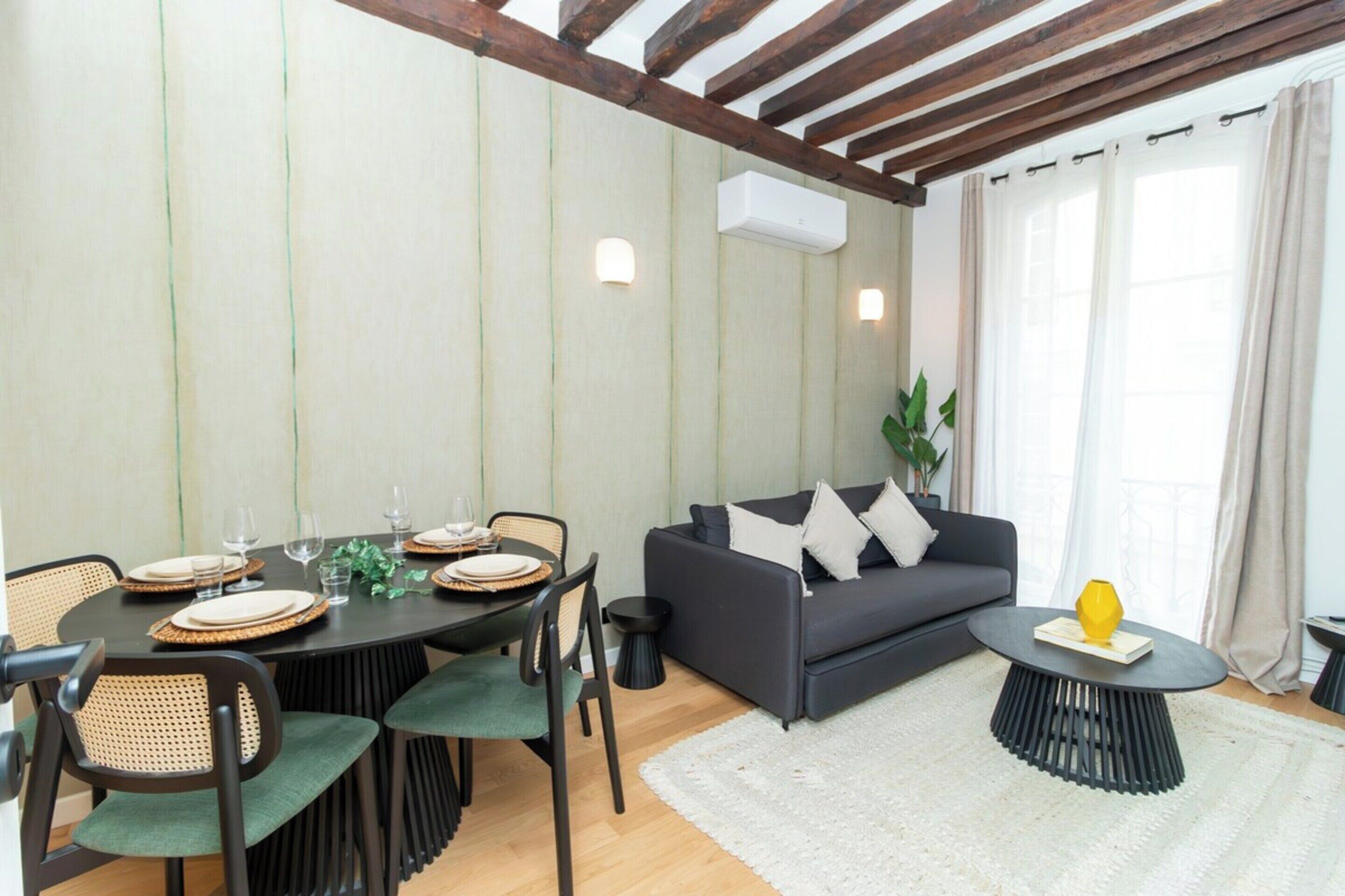 A dining area with a round table set for four, surrounded by chairs. There is a sofa and a coffee table in the living area.