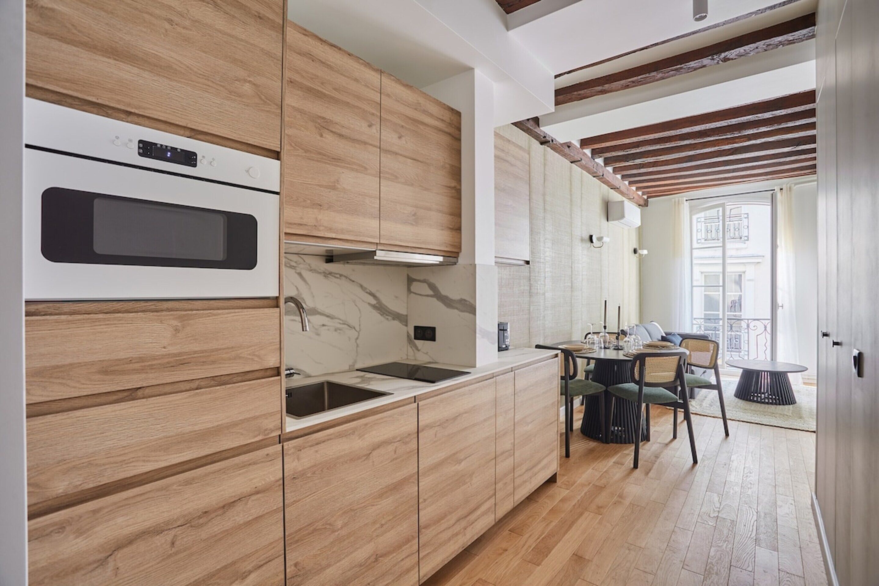 A modern kitchen with wooden cabinets, a built-in oven, and a dining area with a table and chairs.