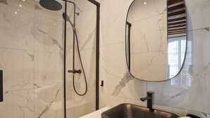 Ein modernes Badezimmer mit einer gläsernen Dusche, einem schwarzen Waschbecken und einem großen Spiegel.