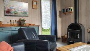 A cozy room with a black leather sofa, a wooden table, a painting on the wall, a clock, a bookshelf, and a wood-burning stove.