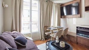 A modern living room with a sofa, dining table, chairs, a TV, and a kitchen area. - New Apartment Center of Paris/le Marais (Paris)