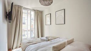 A bedroom with a bed, a window with curtains, a wall-mounted TV, and two framed pictures. - New Apartment Center of Paris/le Marais (Paris)