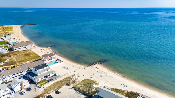 An aerial view of a coastal hotel with multiple buildings, a beach, and a clear blue sea. - Walk to Beach, Steps from Park, Pet-Friendly & Fire Pit (Dennis)