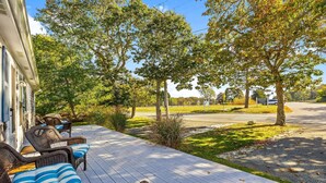A covered porch with wicker furniture and a view of a road and trees. - Walk to Beach, Steps from Park, Pet-Friendly & Fire Pit (Dennis)