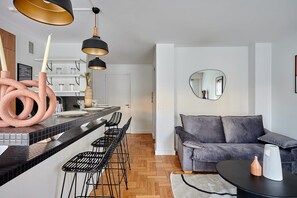 Eine moderne Küche mit schwarzen Barhocker, einem grauen Sofa und einem runden Spiegel.