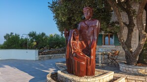 Une statue en bronze représentant un homme et une femme, située dans une cour, avec un bâtiment en arrière-plan.