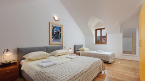 Une chambre avec un grand lit, deux petits lits, un plancher en bois, un tableau au mur et une fenêtre donnant sur un beau paysage.