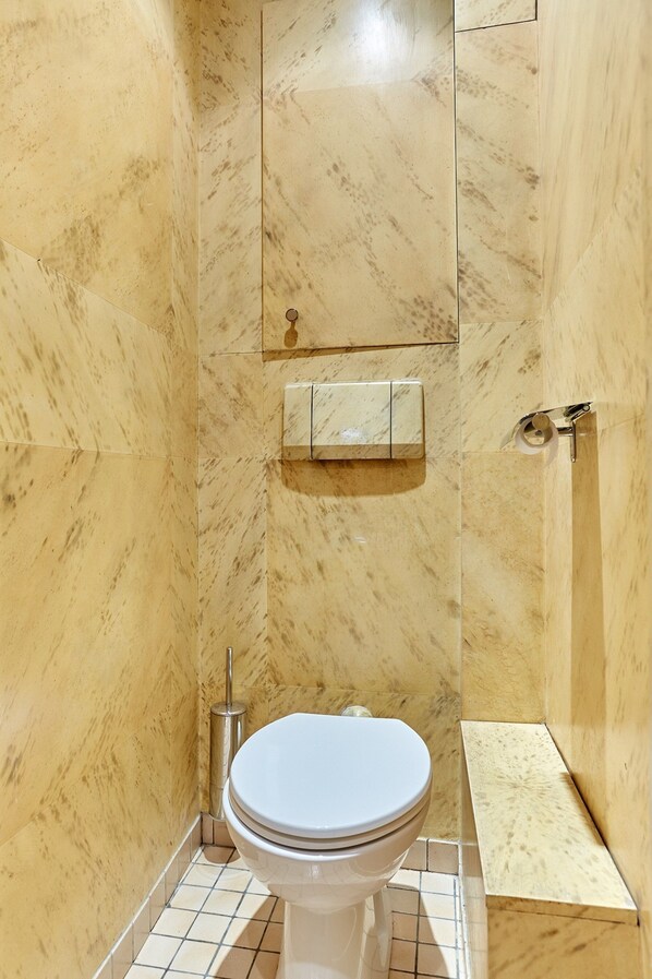 A bathroom with a marble wall, a toilet, a shelf, and a towel rack. - Superb Arc de Triomphe Apartment (Paris)