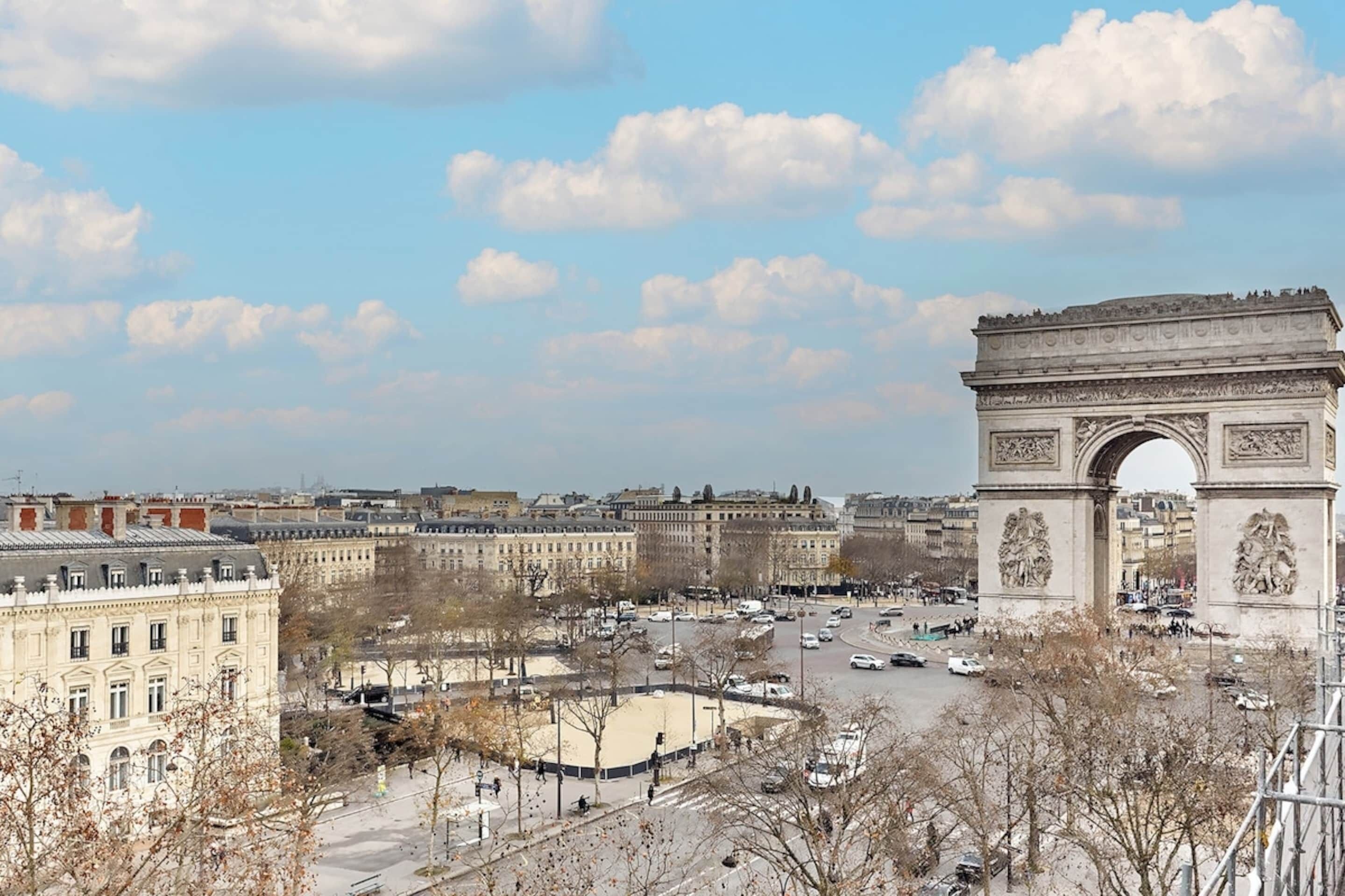 A view of the Arc de Triomphe with surrounding buildings and a busy street.