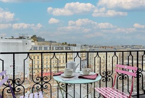 A balcony with a table set for two, a pink chair, and a view of a cityscape. - Superb Arc de Triomphe Apartment (Paris)