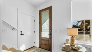 A clean, white interior with a wooden door, a patterned rug, and a table with a lamp and decorative items. - BRAND NEW CONSTRUCTION! CLOSE TO BEACH!  PET FRIENDLY! 3/2 SLEEPS 6! (Panama City Beach)