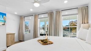 A bedroom with a large bed, a wooden nightstand, a painting, and a window with curtains. - BRAND NEW CONSTRUCTION! CLOSE TO BEACH!  PET FRIENDLY! 3/2 SLEEPS 6! (Panama City Beach)