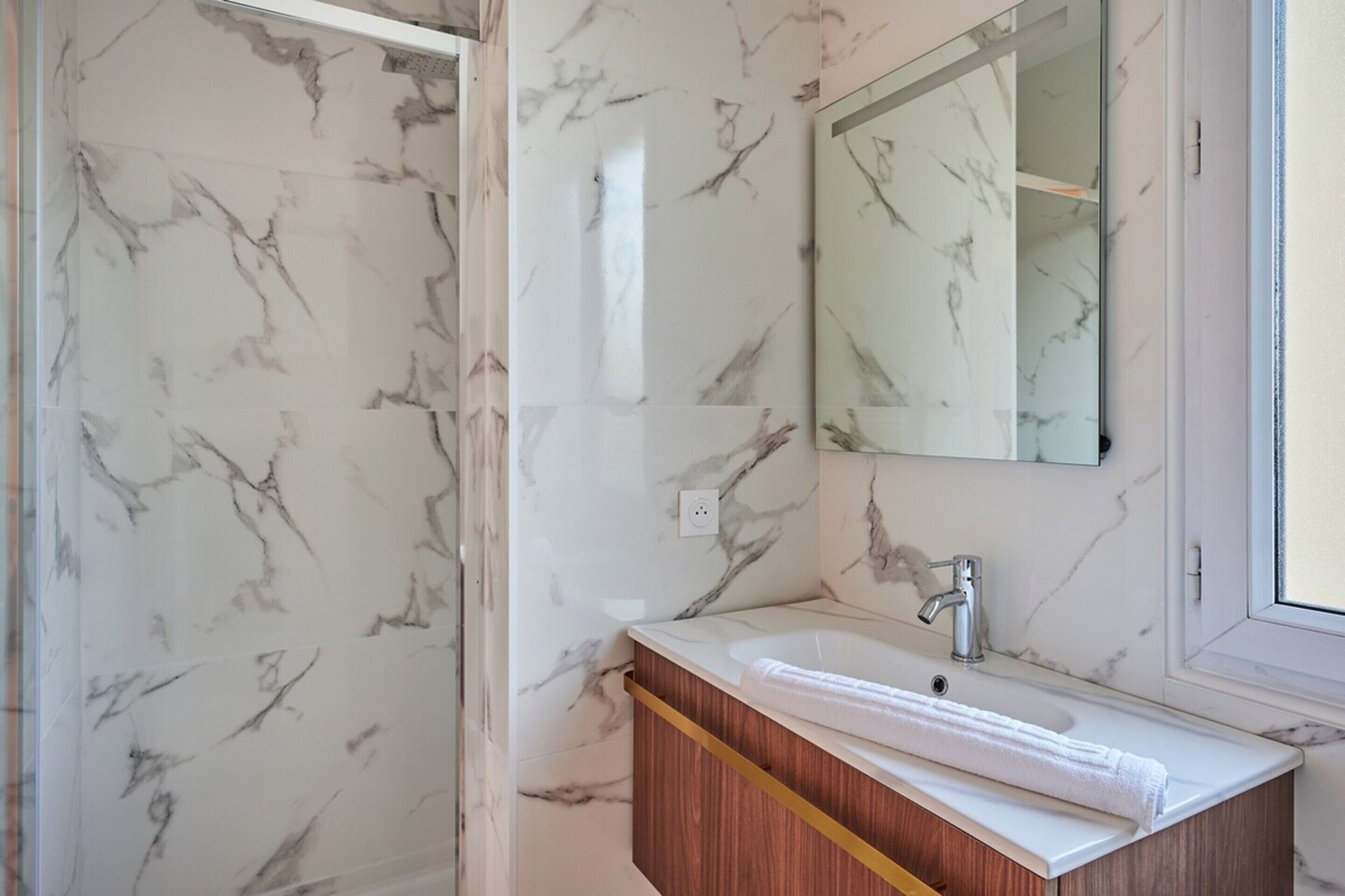 A bathroom with a marble wall, a wooden vanity, a white sink, and a mirror.