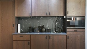 A modern kitchen with wooden cabinets, a marble backsplash, and stainless steel appliances including a kettle, coffee maker, and microwave. - Modern Suite Center of Paris Montmartre (Paris)
