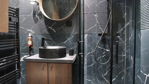 A modern bathroom with a curved glass shower enclosure, a round mirror, and a wooden vanity. - Modern Suite Center of Paris Montmartre (Paris)