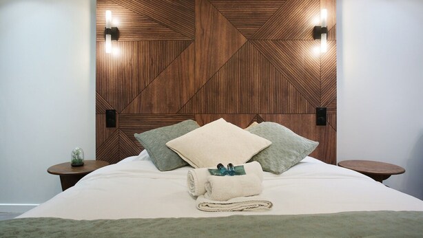 A neatly made bed with a geometric wooden headboard, two bedside tables, and a small decorative item on one table. - Modern Suite Center of Paris Montmartre (Paris)