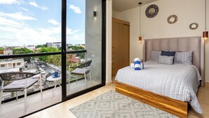 A modern bedroom with a large window, a balcony, and a view of the city.