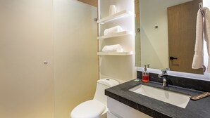 A modern bathroom with a white toilet, a black sink, and a mirror above it. There are shelves with towels and a bottle of soap.