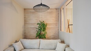 Un soggiorno moderno con un divano chiaro, una lampada a sospensione e un pannello parete in legno.
