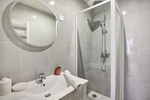 A modern bathroom with a round mirror, a sink, a shower, and a toilet. - Charming Family Apartment - Center of Paris (Paris)