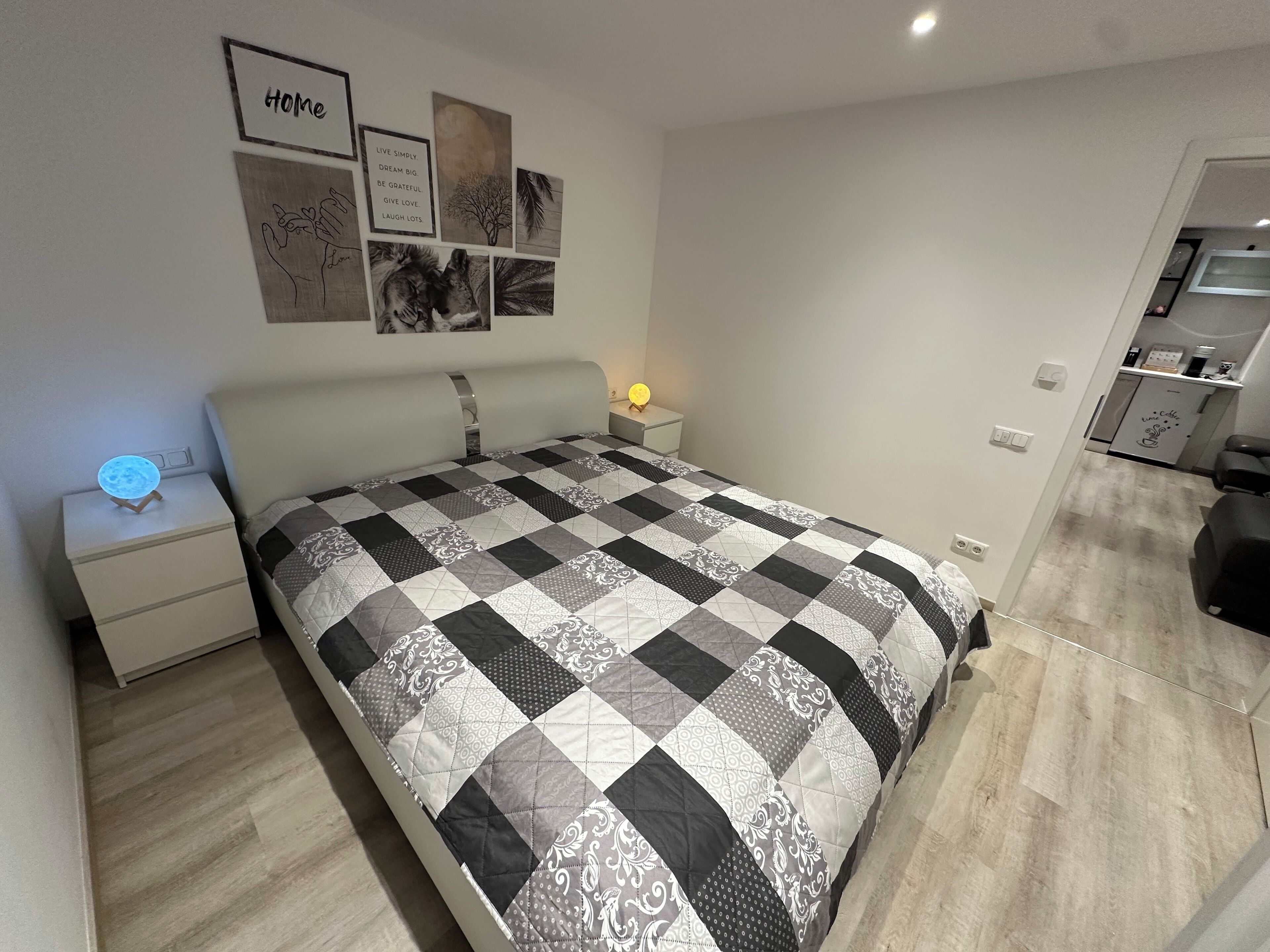 Une chambre moderne avec un grand lit, une table de chevet avec une lampe et un mur orné de citations inspirantes et d’œuvres d’art.