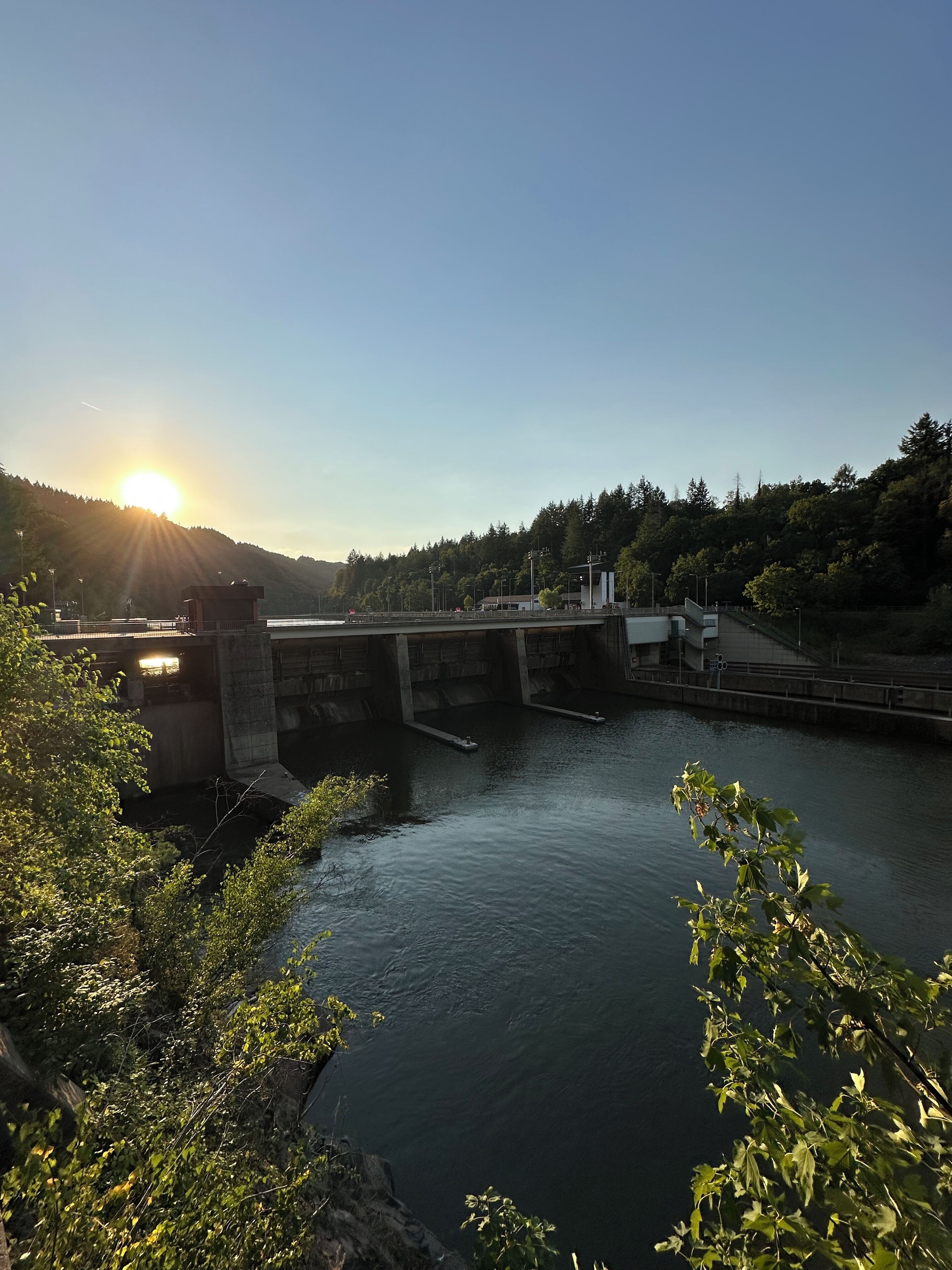 Un río con una presa y un puente, rodeado de árboles y un cielo despejado.