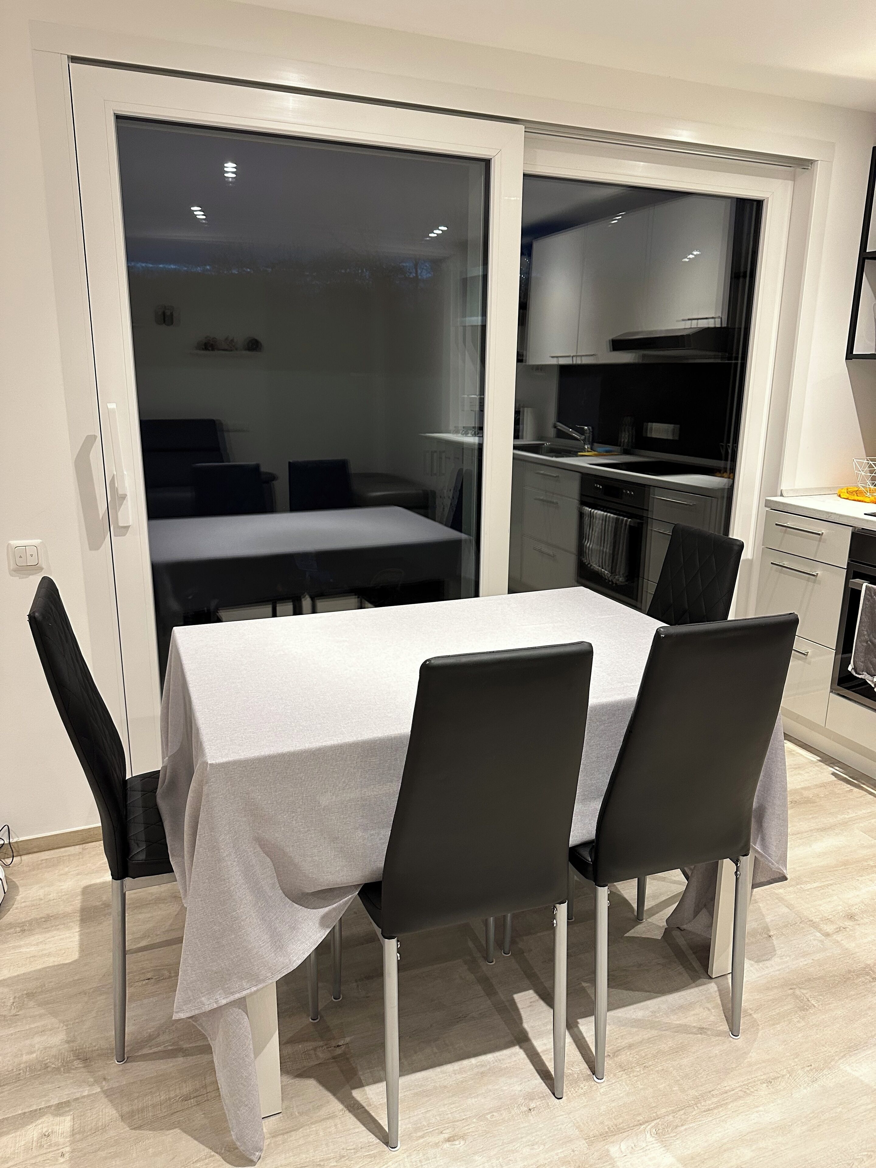 Een moderne eethoek met een tafel en stoelen, een keuken op de achtergrond en een schuifdeur naar een balkon.