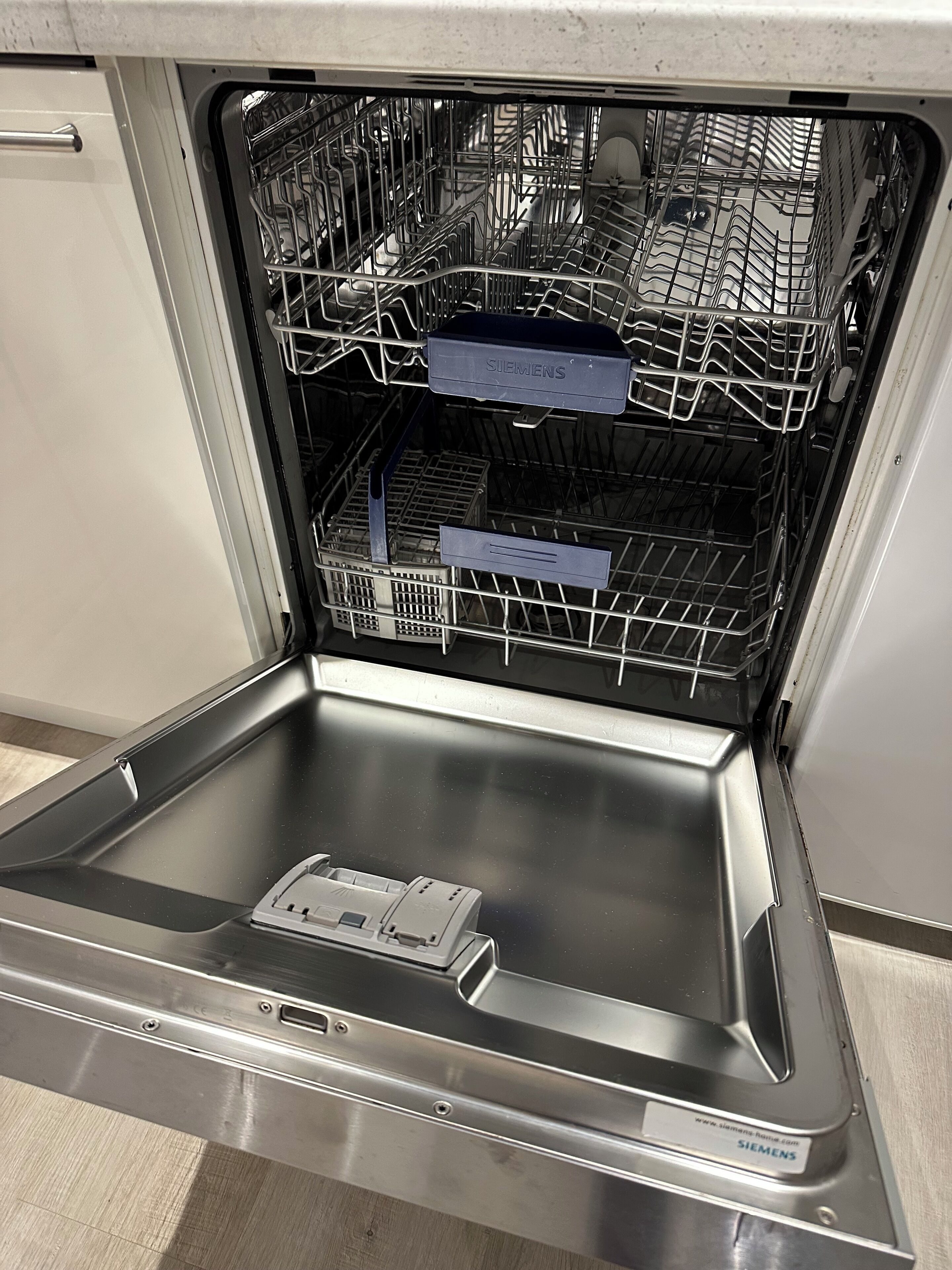 An open dishwasher with a stainless steel interior and a control panel.