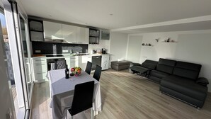 A modern kitchen with white cabinets, a dining table with chairs, and a black sofa in a living area.
