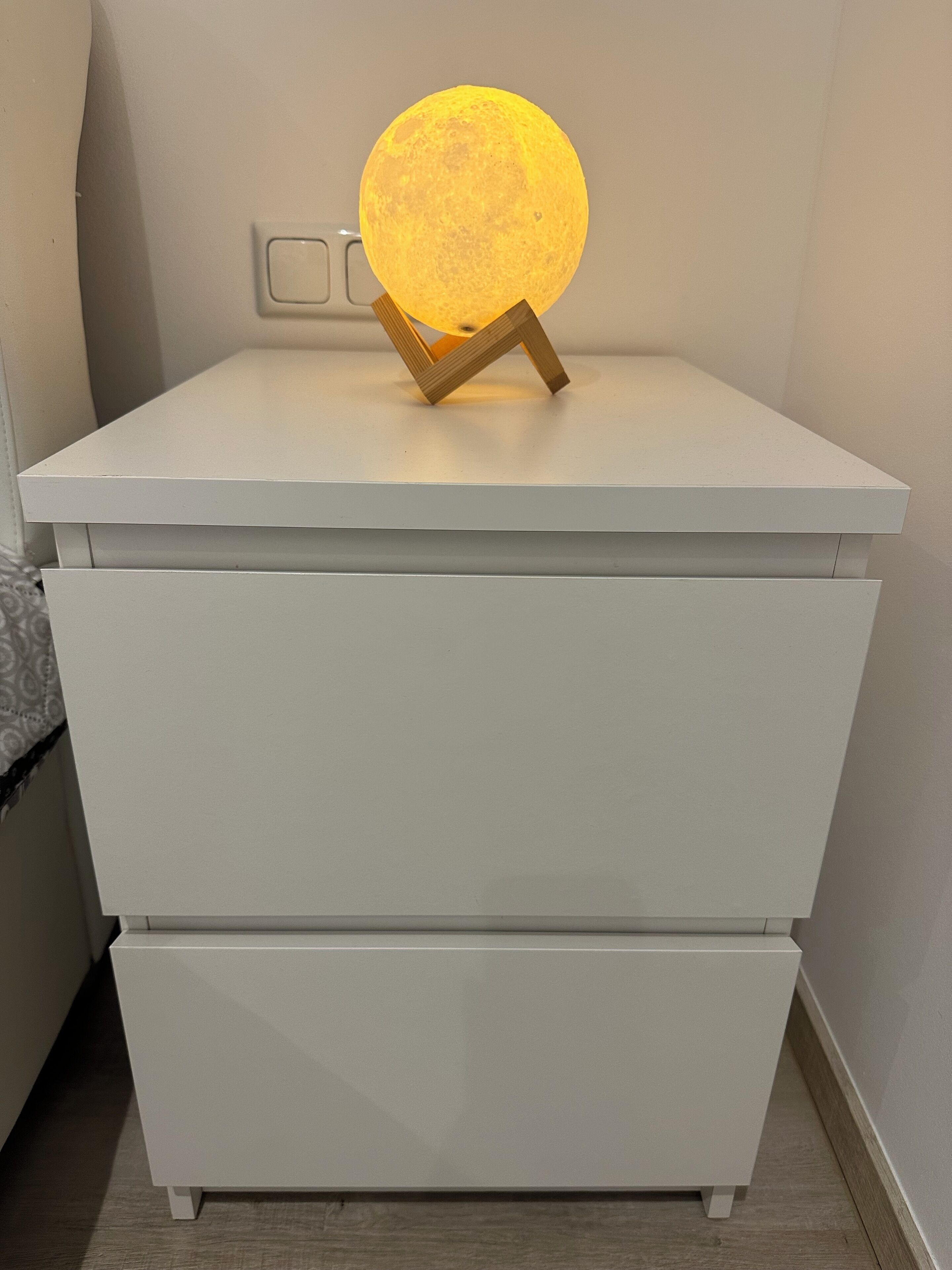 Un comodino bianco con un oggetto rotondo illuminato sopra.