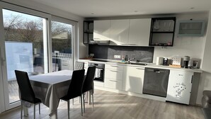 A modern kitchen with a dining area, featuring a large window, white cabinetry, and a coffee machine.