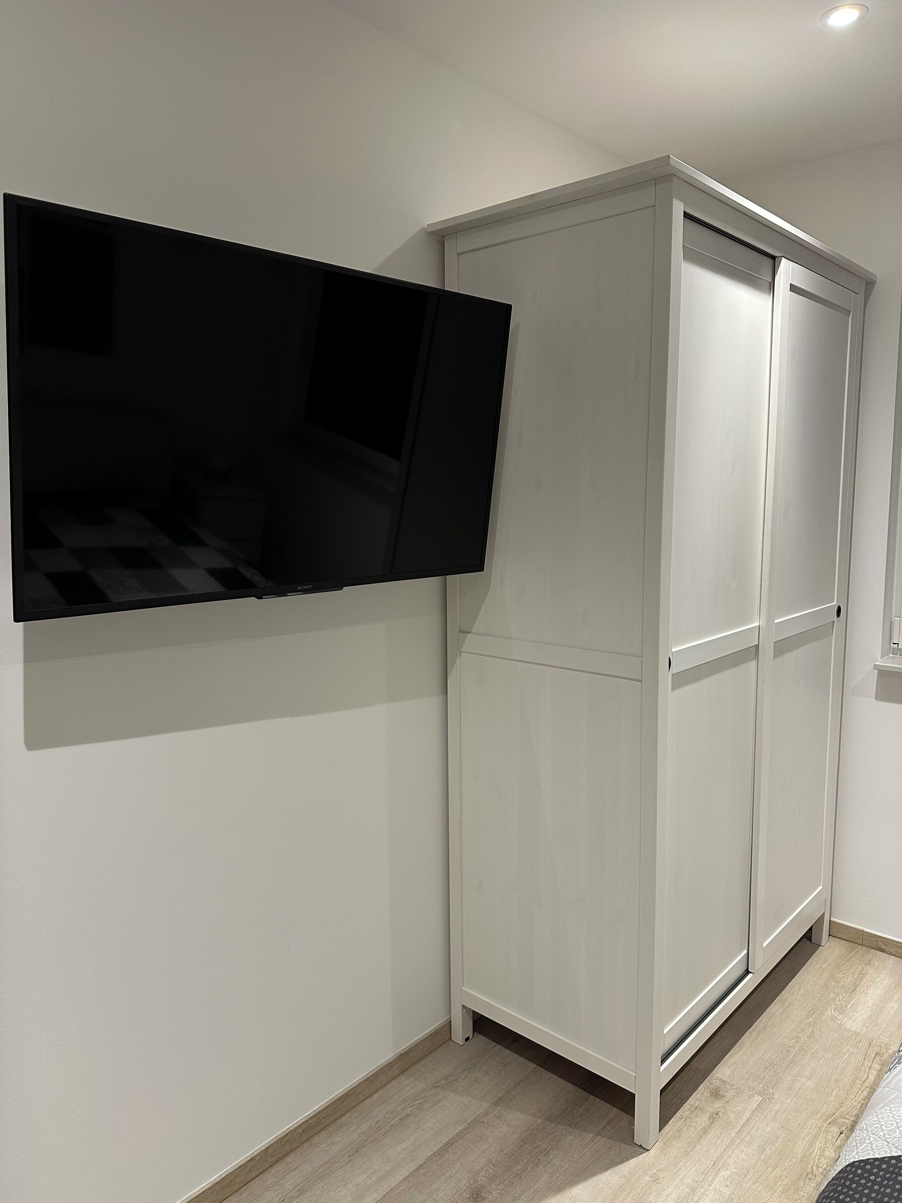 Een kamer met een wandgemonteerde flatscreen-tv, een witte garderobe en een houten vloer.