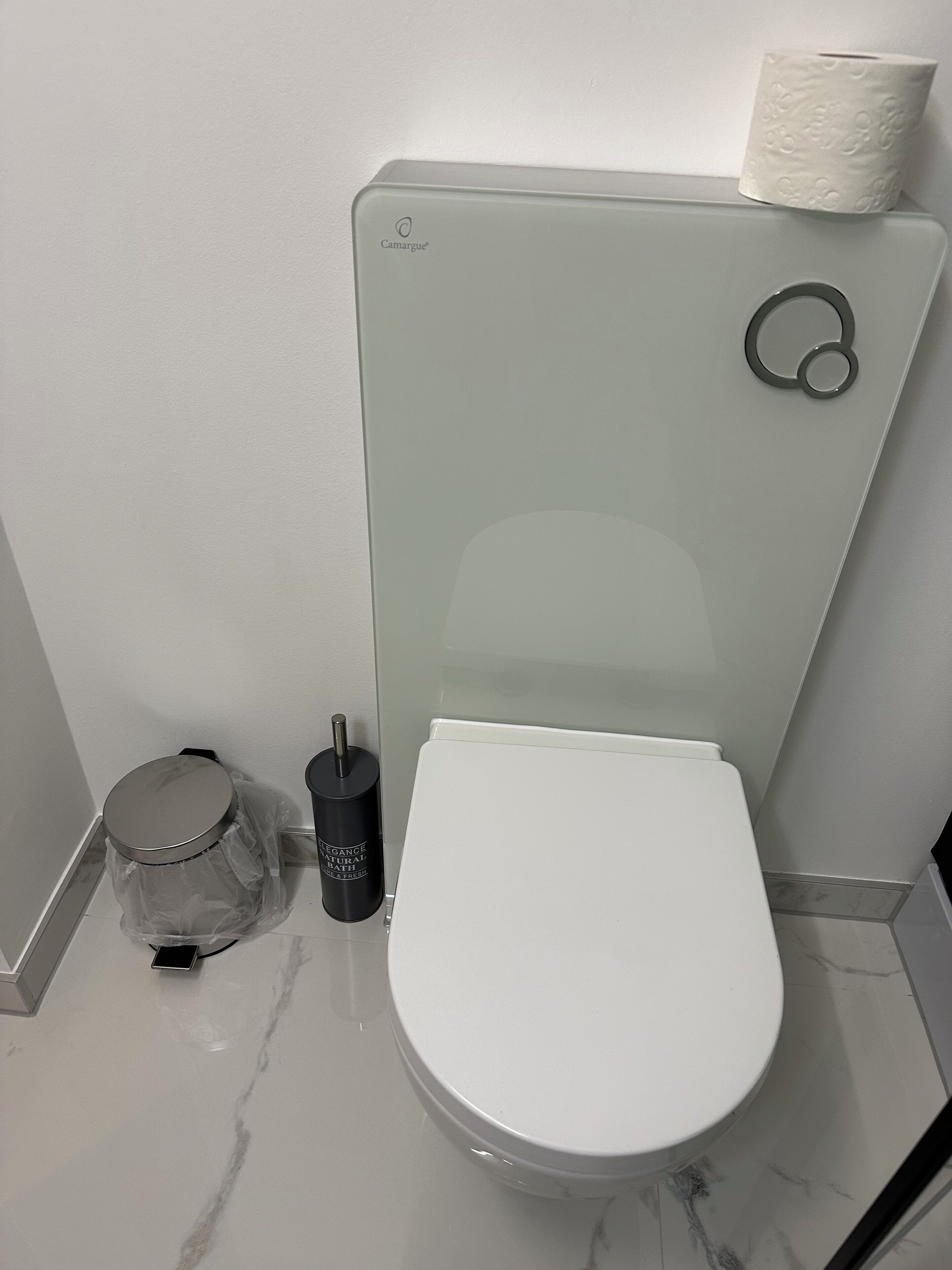 Uma casa de banho moderna com sanita, um contentor de lixo e uma escova de sanita.