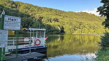 Ein Boot liegt an einem stillen See, im Hintergrund ist ein bewaldeter Hügel zu sehen.