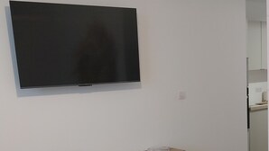 Una sala moderna con un televisor de pantalla plana montado en la pared, un banco de madera y un mueble bajo de color blanco.