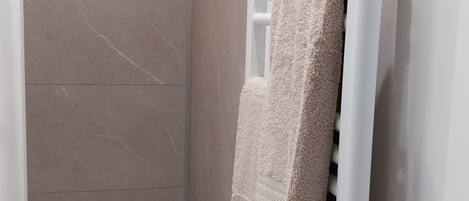 A bathroom with a shower, a towel rack, and a white radiator.