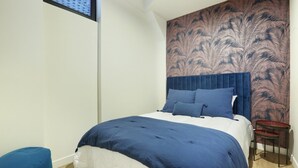 Een slaapkamer met een groot bed, een klein tafeltje en een behang met patroon.
