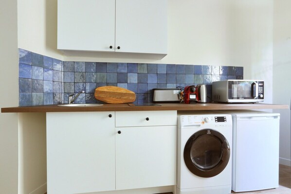 Une cuisine compacte équipée d’un lave-linge, d’un four à micro-ondes et d’une planche à découper en bois posée sur le plan de travail.