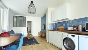Een kleine keuken met een wasmachine, een zithoek met een tafel en stoelen, en een blauwe betegelde spatwand.