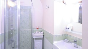 A bathroom with a glass-enclosed shower, a sink with a mirror, and a tiled wall.