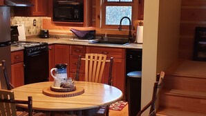 Un interior de madera con una mesa de comedor, sillas, una araña y electrodomésticos de cocina.
