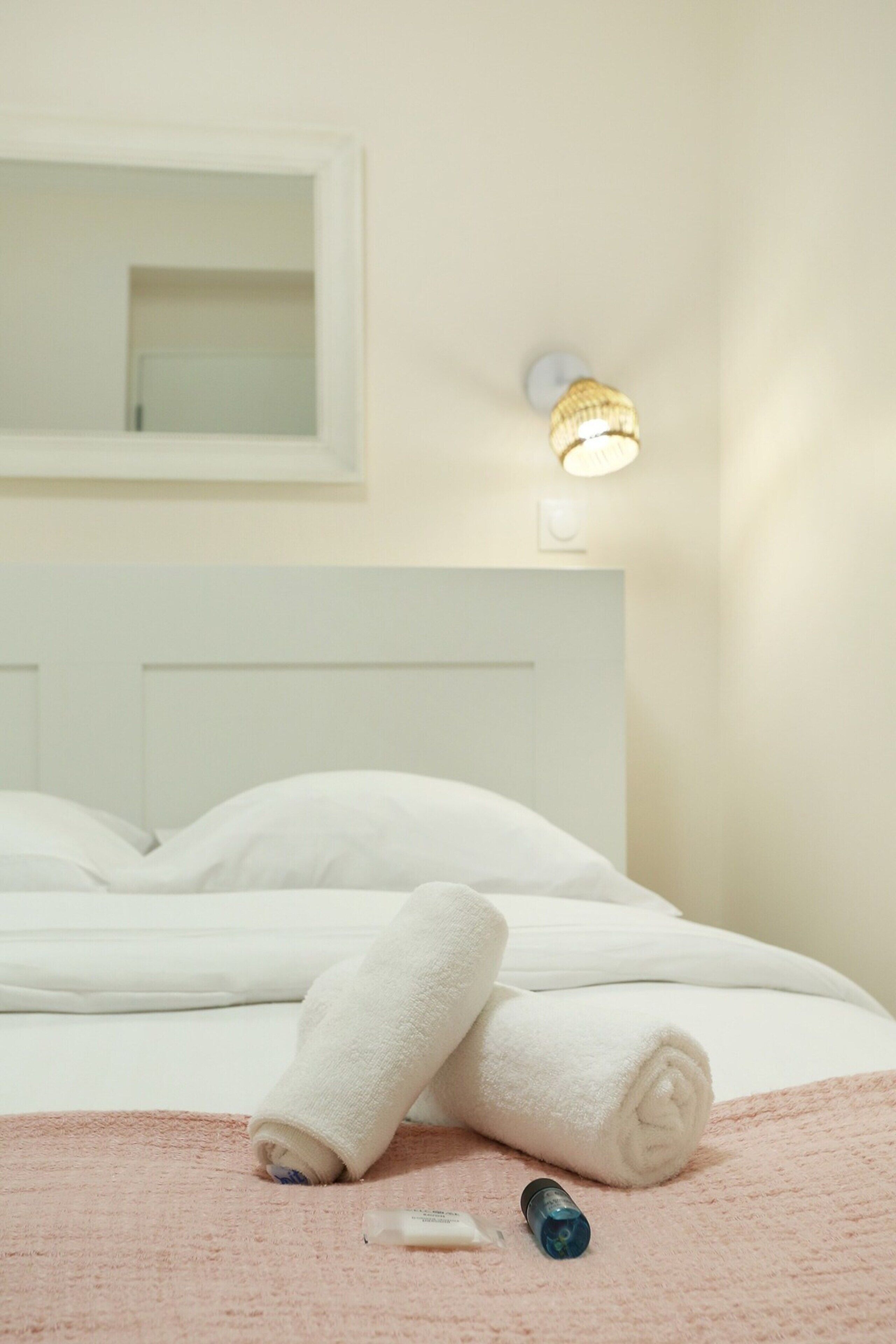 A neatly made bed with a white headboard, a pink towel, and a bottle on the bed.