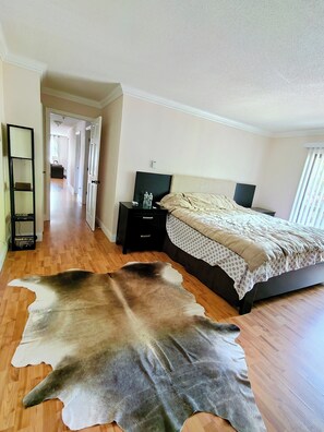 Une chambre à coucher avec un lit, une table de chevet, une grande peau de cuir sur le sol et un couloir menant à une autre pièce.