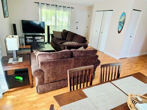 Un salon avec un canapé marron, un téléviseur, une table basse et une table à manger avec des sets de table.