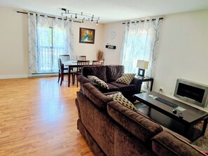 Un salon avec un canapé marron, une table à manger avec des chaises, un téléviseur et une lampe.