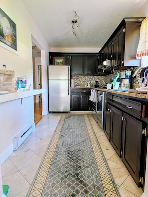 A kitchen with dark cabinets, a stainless steel refrigerator, a tiled backsplash, and a patterned rug.