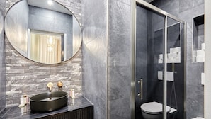 Ein modernes Badezimmer mit rundem Spiegel, Waschbecken in Schwarz und einer Duschkabine aus Glas.