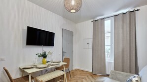 Ein Essbereich mit einem Tisch für vier Personen, einem an der Wand montierten Fernseher und einem Sofa mit Kissen.