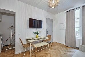 A modern room with a dining table, chairs, a TV mounted on the wall, and a window with curtains.